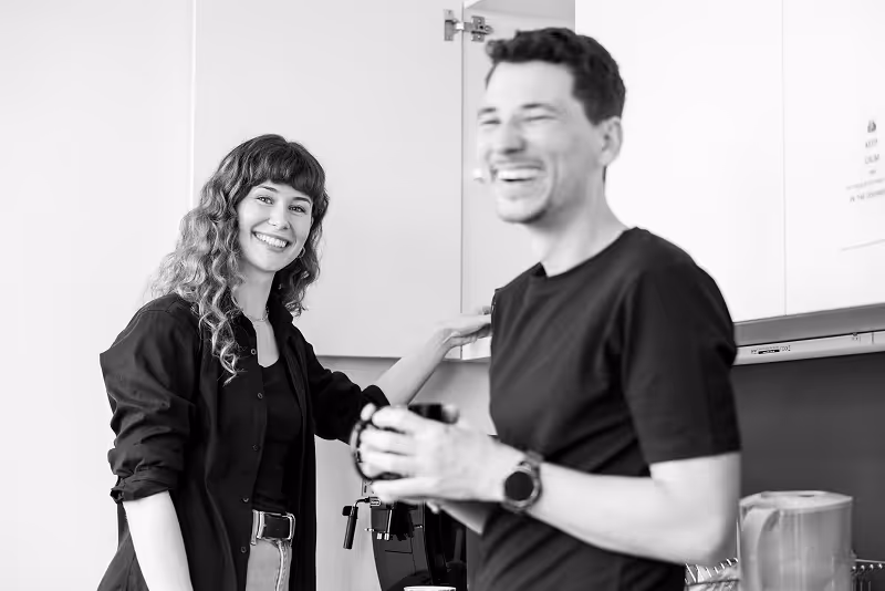 Zwei Kolleg*innen lachen zusammen in der Büroküche.